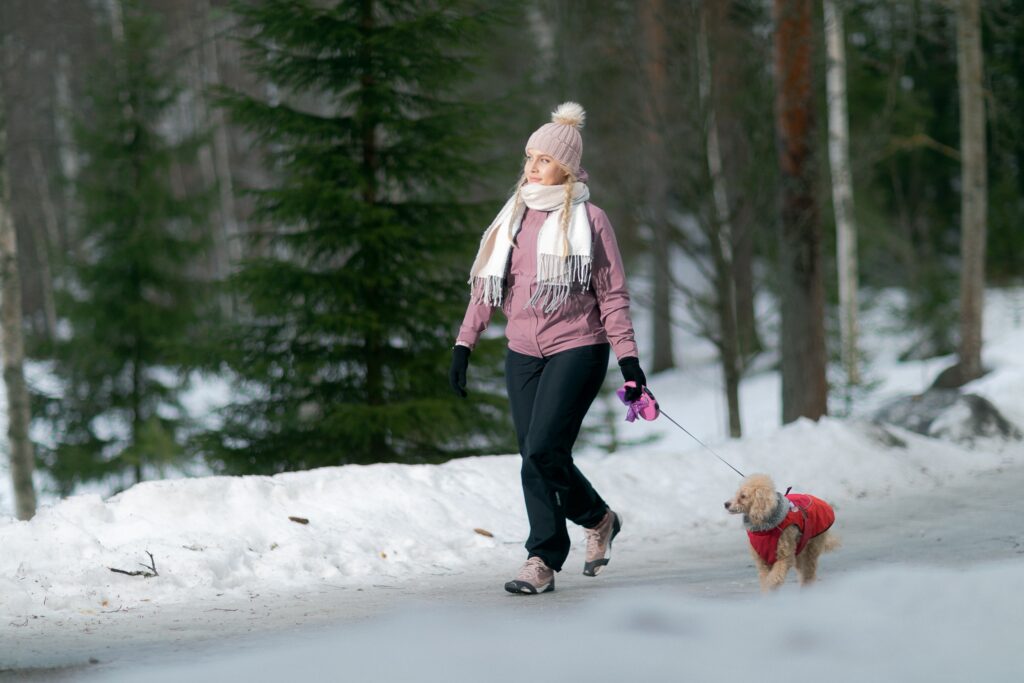 Nainen kävelee koiran kanssa talvisella, liukksaalla tiellä.