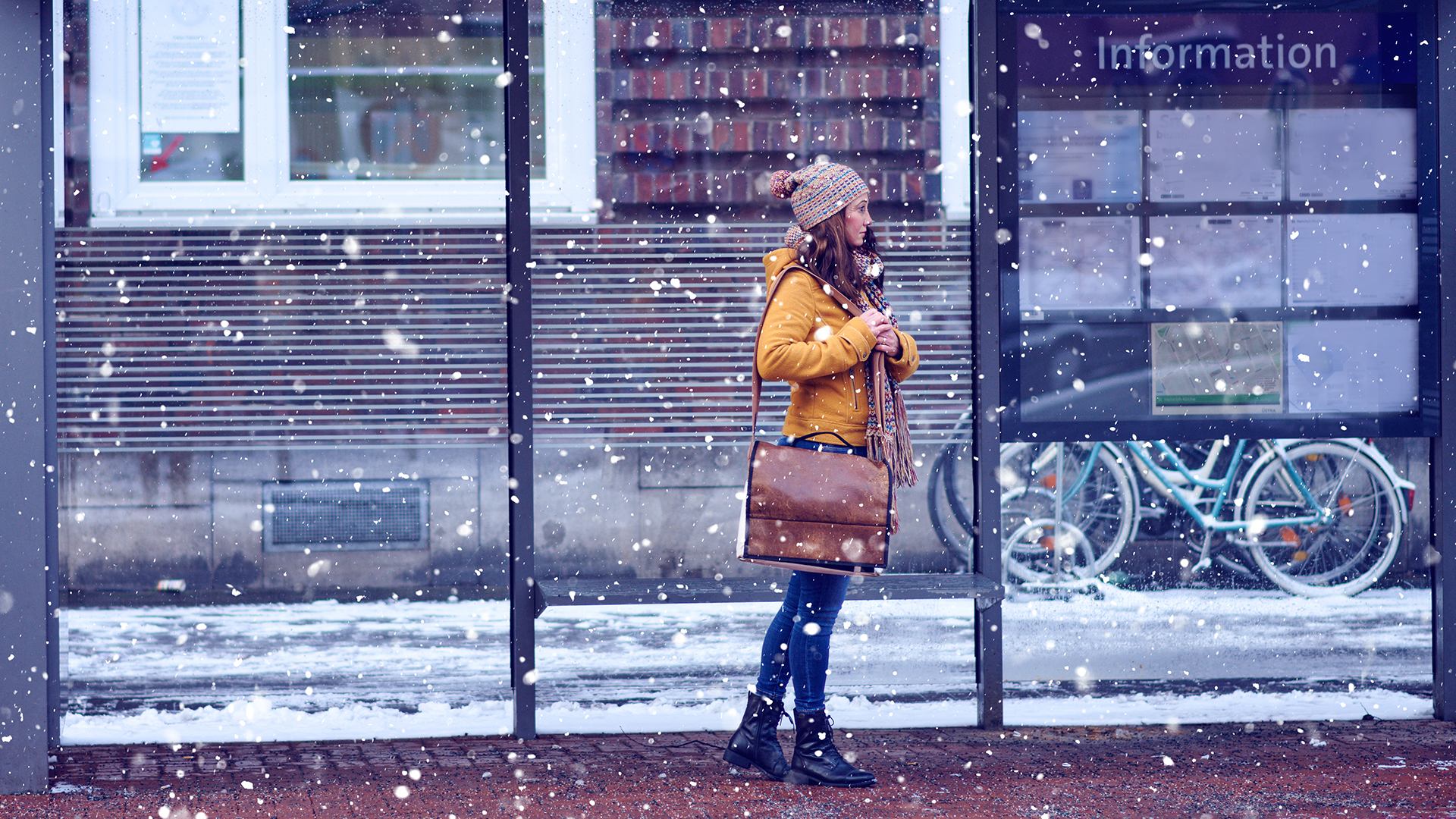 Nainen bussipysäkillä odottamassa bussia lumisateessa
